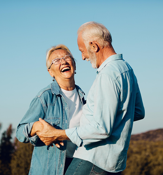 Senior couple laughing together outdoors with dental implants in Alexandria