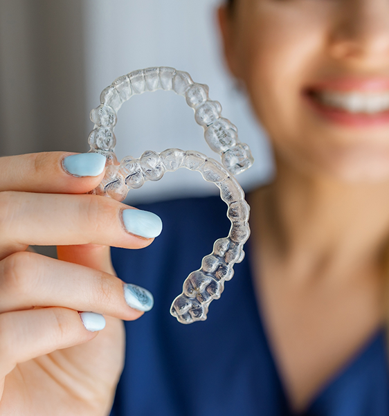 Smiling dentist holding two Invisalign clear aligners in Alexandria