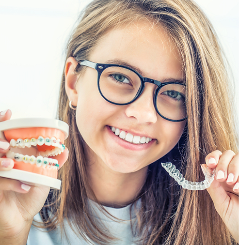 Young woman holding an Invisalign aligner in one hand and a model of the teeth with braces in the other hand
