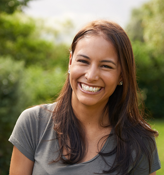 Brunette woman grinning outdoors after restorative dentistry treatment
